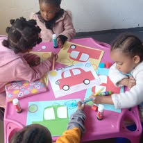 Busy Bees toddlers decorating pictures of vehicles at a table at Twinkle Toes