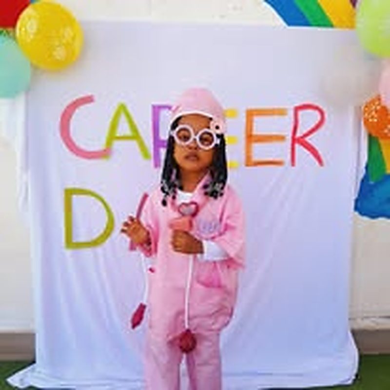 Child dressed in a doctor's outfit in front of a career day backdrop at Twinkle Toes
